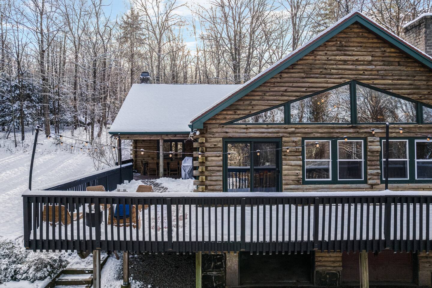 Snow-covered cabin with a wooden deck in a forested area.
