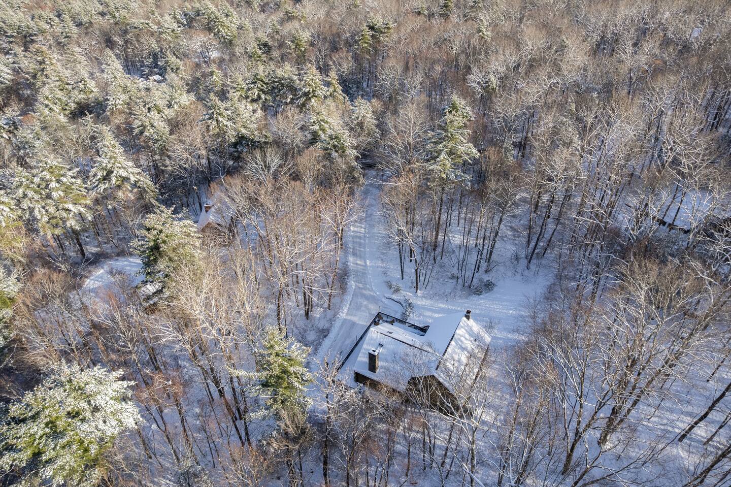 Snow-covered cabin with a wooden deck in a forested area.